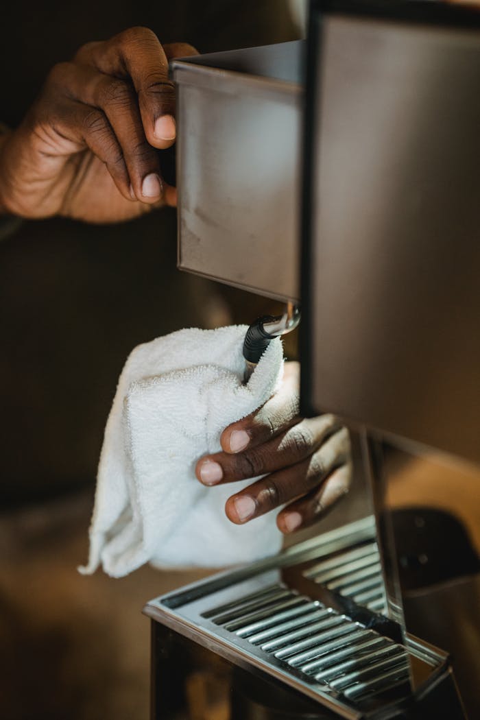 Close-up of a man cleaning a coffee machine with a white cloth, focusing on hygiene.